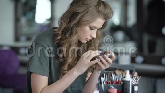 美容店里的女孩金发女郎坐在椅子上通过电话看新闻这女人已经化妆了视频的预览图