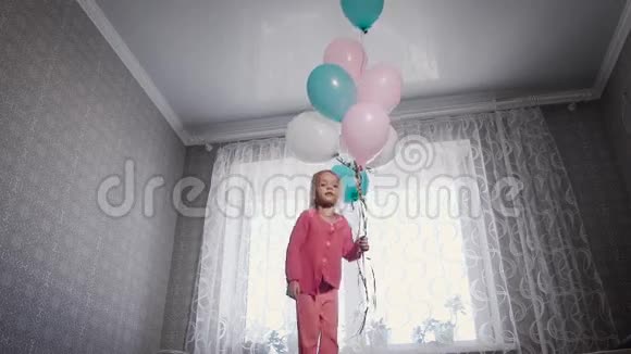 一个金发的小女孩穿着一件粉红色的衬衫裤子在床上跳站在窗前视频的预览图