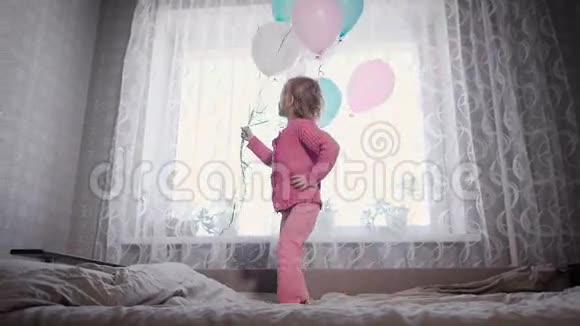 快乐的小女孩跑在托儿所的床上的窗户附近手里拿着一堆气球视频的预览图