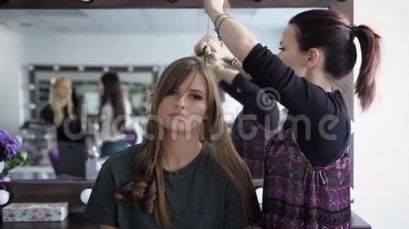 理发师在漂亮女孩的头发上做一个波纹然后她会用熨烫使它们卷曲在模特化妆上视频的预览图