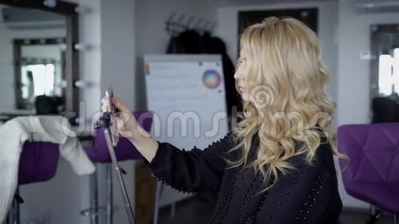 一个年轻的女人在完成她的发型后在豪华美容院关闭有长卷发的女士拿着自拍视频的预览图