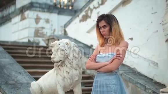 穿着银色和蓝色连衣裙的漂亮女孩站在楼梯上石栏杆靠近狮子雕像手臂交叉着视频的预览图
