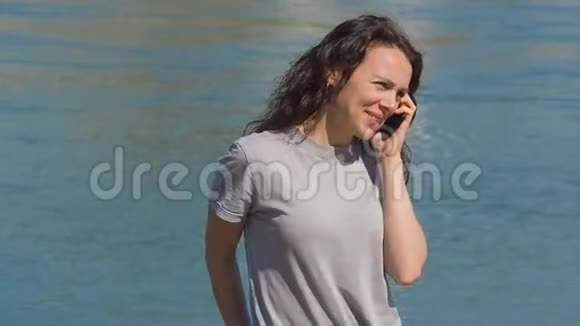 水边拿着手机的女孩一个女人在晴天河堤上打电话视频的预览图