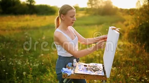 美丽的金发女画家手拿画笔在大自然的画布上画画视频的预览图