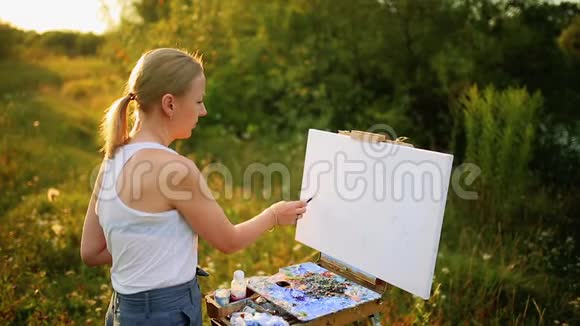 美丽的金发女画家手拿画笔在大自然的画布上画画视频的预览图