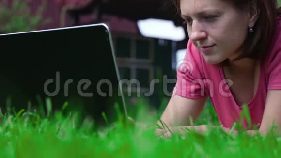 女孩用笔记本电脑躺在草坪上视频的预览图