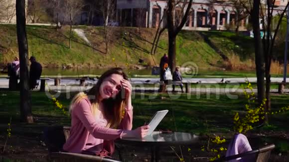 漂亮的女孩近脸休息在春天公园与平板电脑和看相机视频的预览图