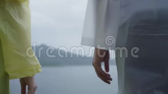年轻的亚洲甜蜜情侣在浪漫的时光里玩雨穿着雨衣站在湖边感觉很幸福视频的预览图