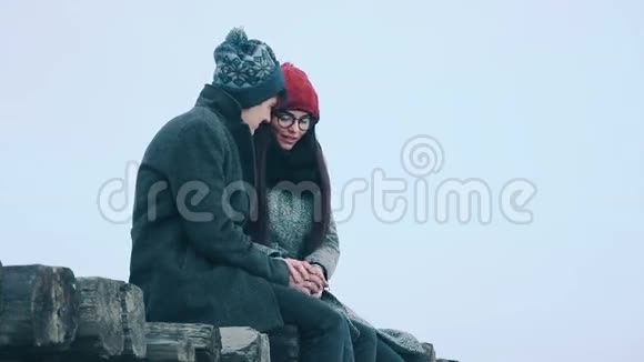 可爱的夫妇坐在一座木桥上在灰色的雪天背景上交谈着视频的预览图