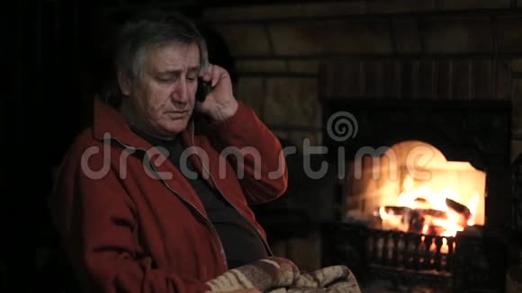 坐在壁炉旁的椅子上用手机说话的老人视频的预览图