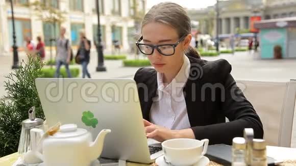 有笔记本电脑的咖啡馆里的女商人她喝咖啡看新闻视频的预览图