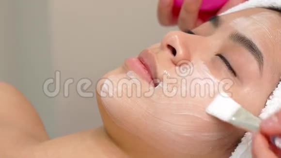 美容专家用刷子在女孩的脸上涂化妆品面膜视频的预览图