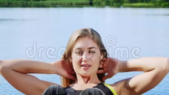 美丽的运动的年轻金发女人伸展摆动压力湖河蓝天和森林的背景视频的预览图