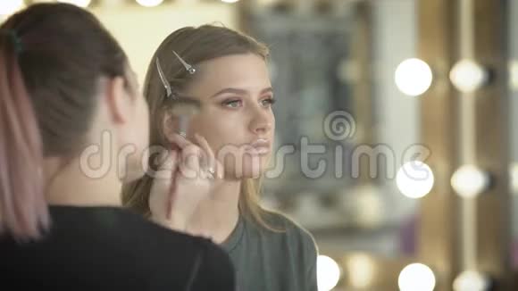 美容店里的女孩化妆大师训练这位漂亮的女孩做一个球化妆师用刷子视频的预览图