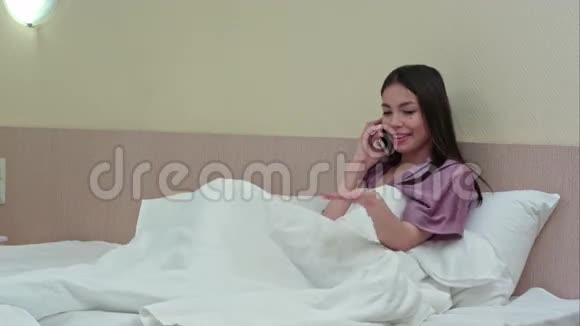 在卧室的床上有电话交谈的快乐年轻女人视频的预览图