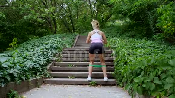 美丽的运动年轻金发女人跑楼上在森林公园在夏天进行练习视频的预览图