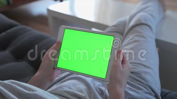 美丽的年轻女子正在使用一个数字平板电脑绿色屏幕坐在沙发上在家里视频的预览图
