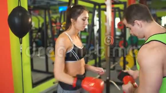 拳击教练男子帮助健身俱乐部的年轻女子戴上拳击手套视频的预览图