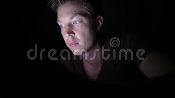 年轻英俊的斯堪的纳维亚人在黑暗的房间里使用数字平板电脑视频的预览图