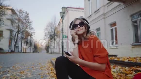 可爱的少女听耳机音乐都市风格时髦的时髦少女坐在城市街道的人行道上视频的预览图