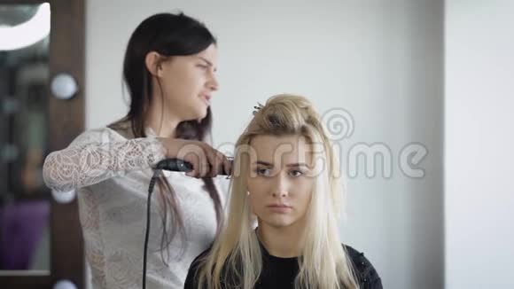 在理发店里一个新的模特坐在头发上它把铁放在头发的根部做卷发这个视频的预览图