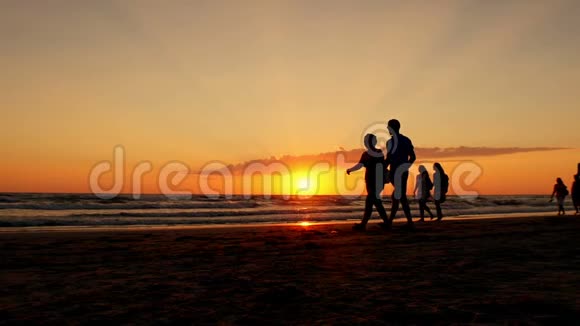 在海浪和红日落的背景下人们沿着海边散步的剪影视频的预览图