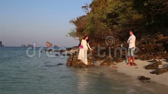 新娘坐在岩石上新郎日出时从海滩上看视频的预览图