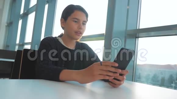 十几岁的女孩在餐桌上的一家咖啡馆里用智能手机的生活方式聊天交流视频的预览图