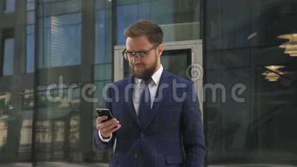 英俊的商人正在使用智能手机站在办公楼的背景上视频的预览图