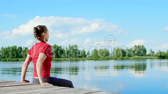 美丽的运动的年轻金发女人伸展做俯卧撑湖河蓝天和森林的背景视频的预览图