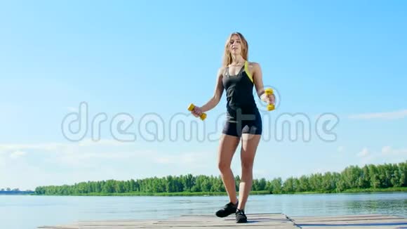 美丽的运动的年轻金发女人做不同的运动与重量哑铃弓步蹲湖泊河流视频的预览图