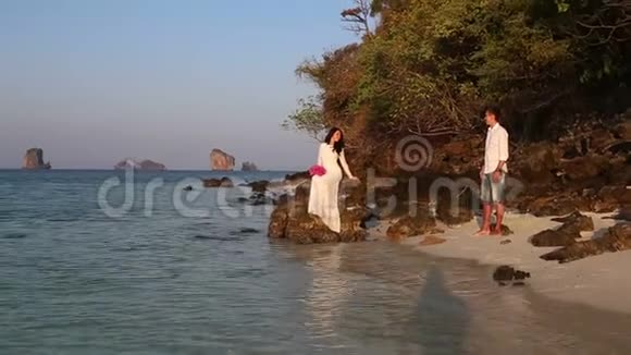 新娘坐在岩石上新郎日出时从海滩上看视频的预览图