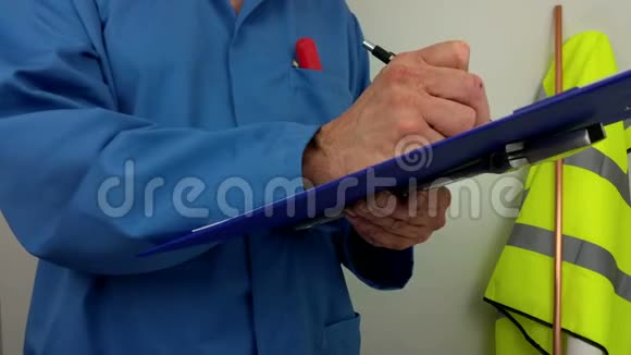 穿蓝色工作服的水管工在剪贴板上写报告视频的预览图