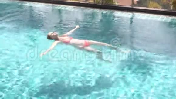 幸福快乐的年轻女子在红色的游泳套房里躺在游泳池里的水上晴朗的天气视频的预览图