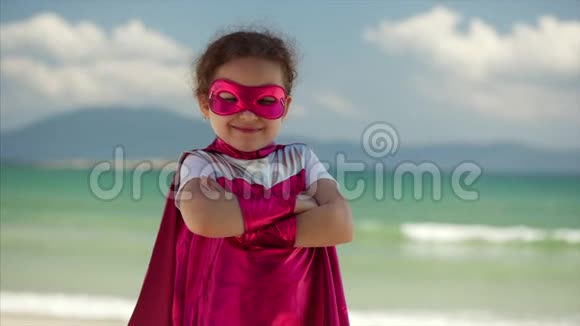 美丽的小女孩穿着超级英雄的服装穿着粉红色的斗篷和英雄的面具坐在飞机上视频的预览图