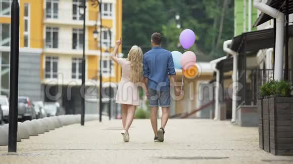 年轻夫妇牵着手走在街上男人拿着气球浪漫视频的预览图