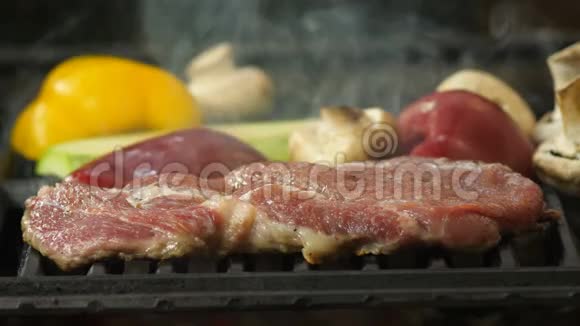 牛肉猪肉或小牛肉牛排放在烤架上背景是烤架上的烟雾和烤蔬菜背景是视频的预览图