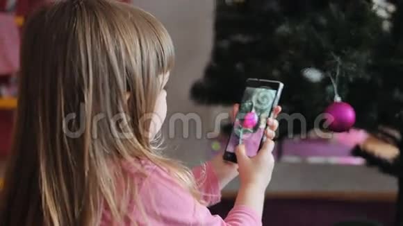小女孩在家里的客厅里用手机拍照圣诞树上有节日的灯光视频的预览图