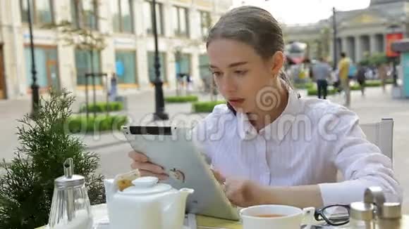 有平板电脑的咖啡馆里的女商人她喝咖啡看新闻视频的预览图