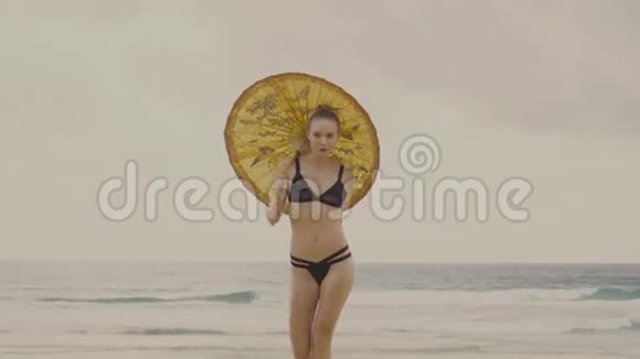 性感迷人的女人穿着黑色比基尼在海滩上打着中国伞视频的预览图