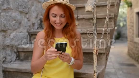 红发女游客在古城街道上使用智能手机视频的预览图