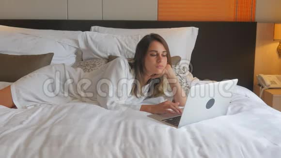 穿着浴袍躺在床上手提电脑工作的年轻女子视频的预览图