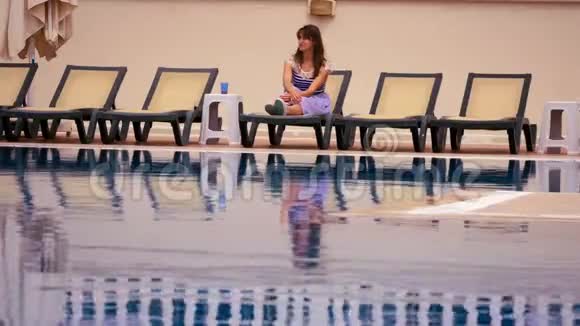 年轻女子坐在沸腾的游泳池旁视频的预览图