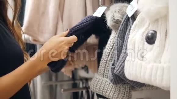 年轻的混血女人在购物中心的服装店挑选编织的冬帽4K视频的预览图
