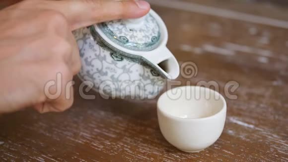 男性手浇健康绿茶从茶点在复古杯上的木制桌子传统仪式概念视频的预览图