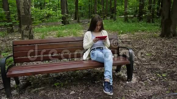 美丽的少年女孩带着平板电脑坐在公园的长凳上静态相机的电影视频的预览图