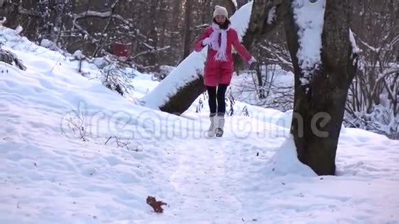 在白雪皑皑的冬林中一个穿着红色夹克的美丽快乐女孩向镜头奔跑的慢镜头视频的预览图