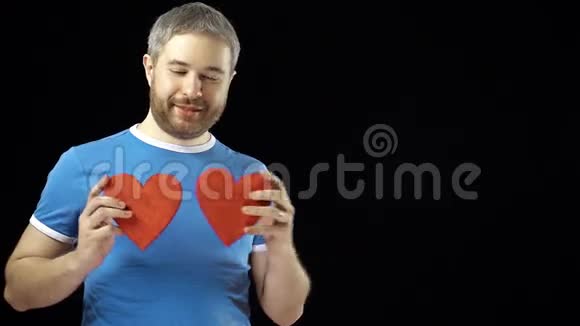 穿蓝色t恤的快乐男人有两个红色的心形爱情浪漫约会关系概念黑色背景4K视频的预览图