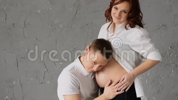 英俊的年轻人听着他怀孕妻子的肚子年轻的妻子拍拍他的头笑吧慢动作视频的预览图