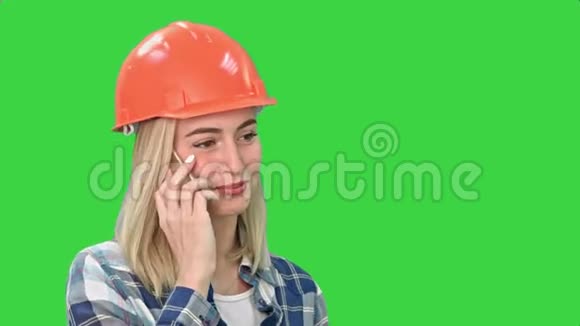 美丽的快乐女人在橙色硬帽有一个电话通过智能手机和微笑的绿色屏幕Chroma键视频的预览图